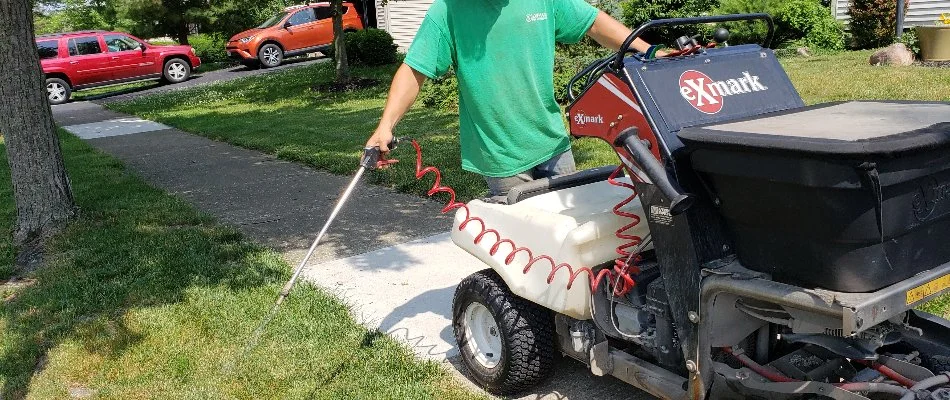 A professional in Delaware, OH, spraying weeds near a sidewalk.